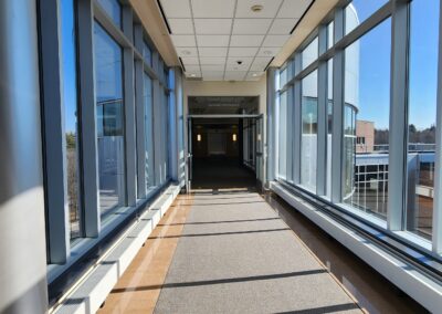 Light falling from right to left through floor to ceiling windows along a carpeted hallway leading to a dark area. The effect makes it seem as if the hallway is entirely open.